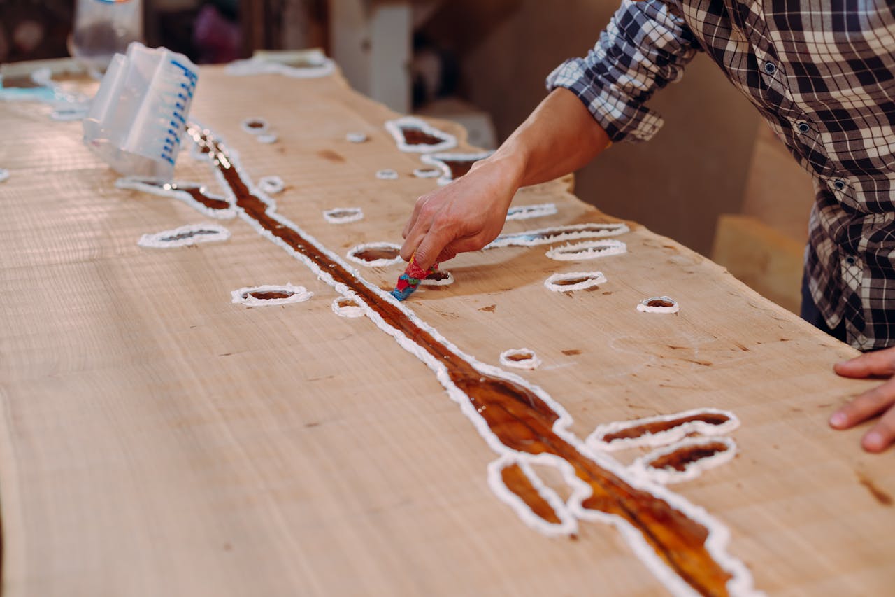 A skilled craftsman applying resin on a wooden table in a workshop setting.